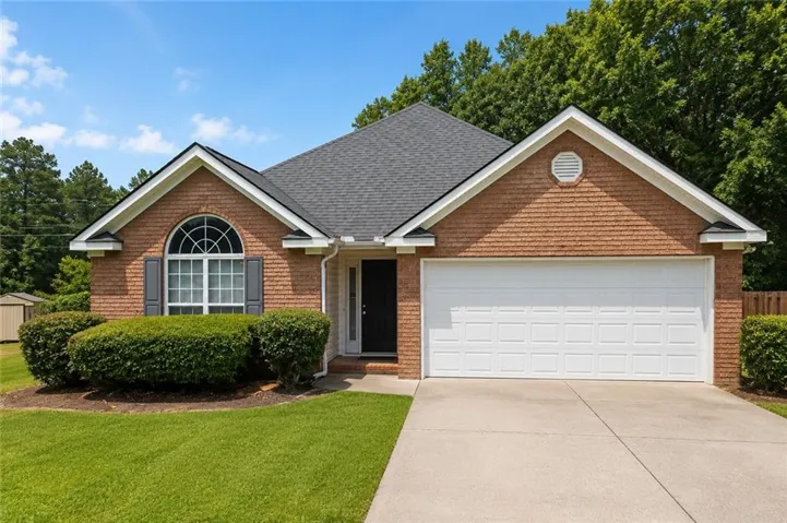 Brick facade home featuring a two-car garage, arch-top window with shutters, dark asphalt shingle roof, and a meticulously manicured lawn