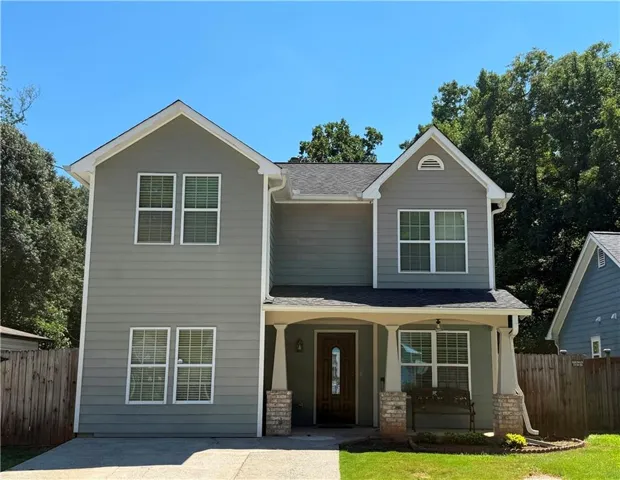 Two-story residence featuring light gray siding, white window trim, a covered porch with stone-clad columns, and a dark wood-finish front door