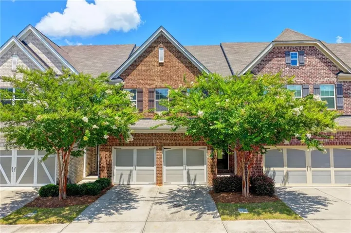 Traditional brick and siding townhome featuring a gabled roofline, multiple windows with dark shutters, and a two-car garage