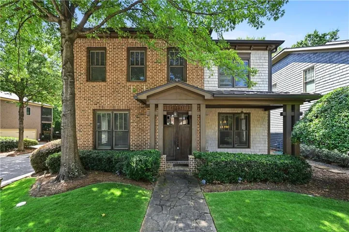 Brick and shingle exterior with a covered entry, dark wood-finish front door, and established landscaping
