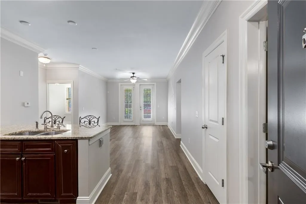 Kitchen featuring crown molding, dark wood-style flooring, light stone counters, ceiling fan, and open floor plan