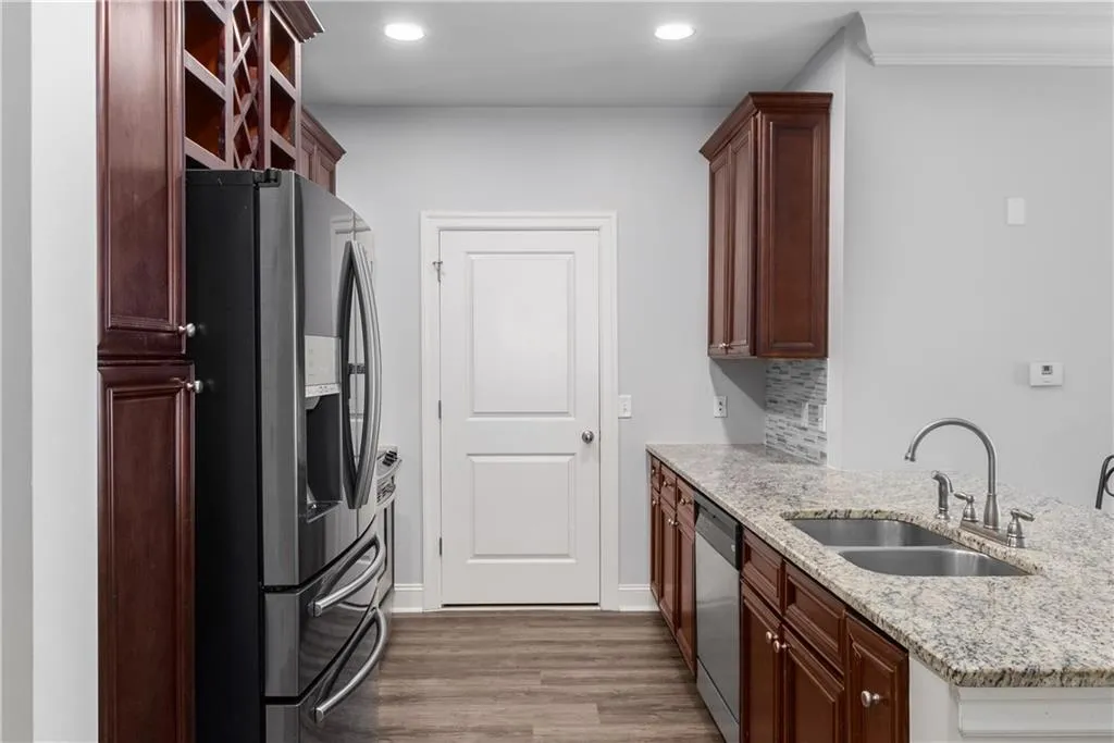 Kitchen featuring appliances with stainless steel finishes, a peninsula, dark wood-style flooring, light stone counters, and backsplash