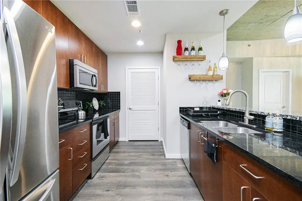 Kitchen featuring appliances with stainless steel finishes, wood finished floors, decorative backsplash, dark stone counters, and decorative light fixtures
