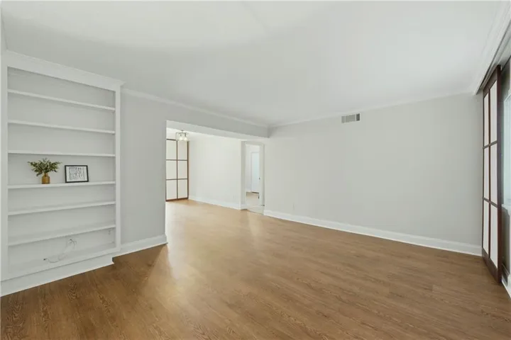 Spacious interior featuring wood-finish flooring, built-in shelving, crown molding, and large window panels
