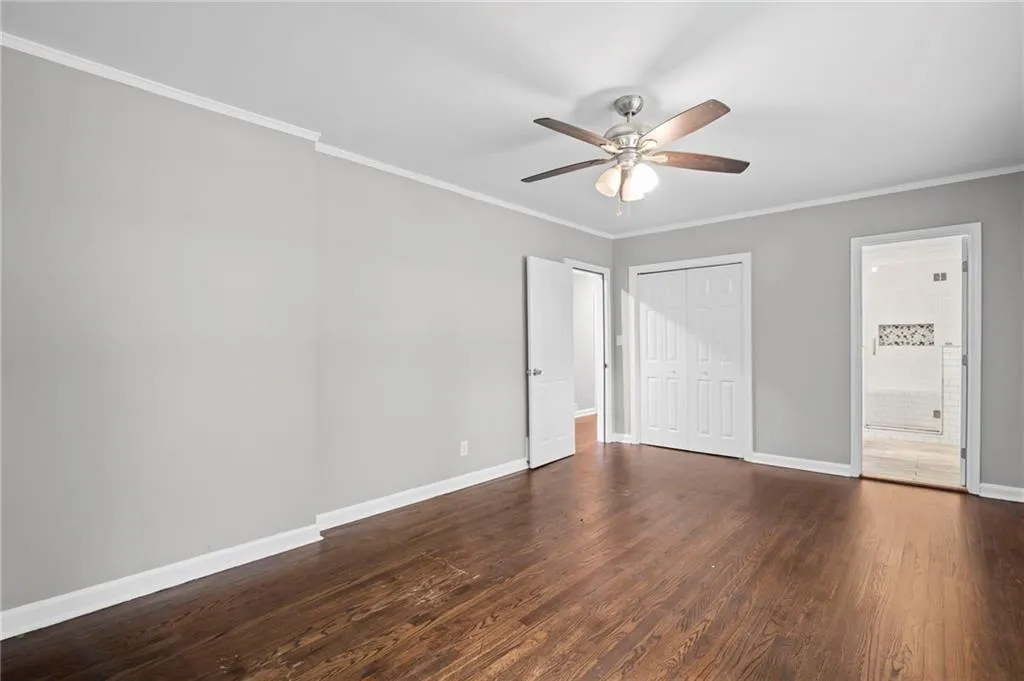 Unfurnished bedroom with ornamental molding, dark wood-type flooring, a ceiling fan, a closet, and connected bathroom
