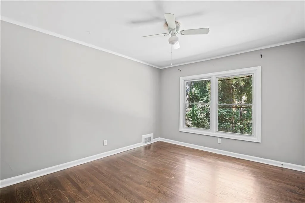 Empty room with ornamental molding, dark wood-style flooring, and ceiling fan