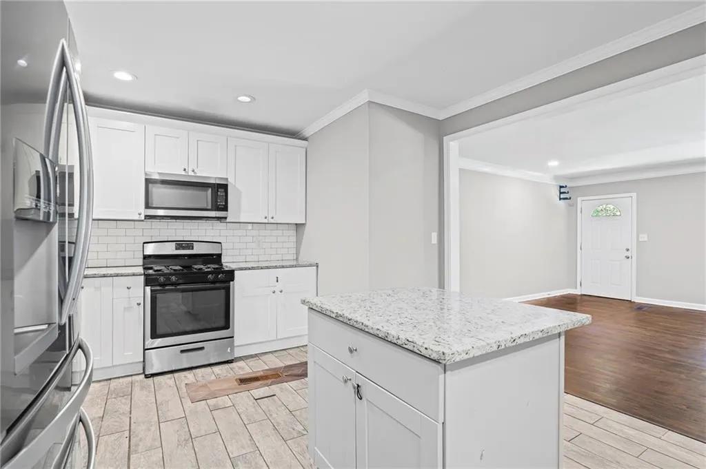 Kitchen with appliances with stainless steel finishes, decorative backsplash, white cabinetry, light wood finished floors, and recessed lighting