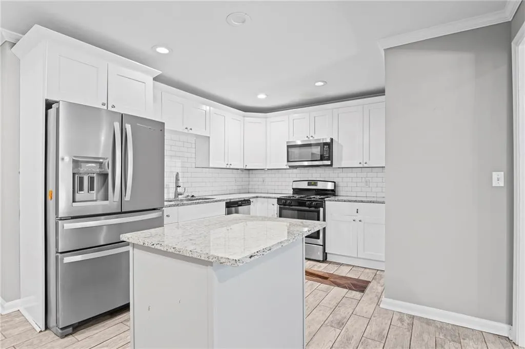 Kitchen featuring decorative backsplash, wood finish floors, appliances with stainless steel finishes, white cabinetry, and light stone countertops