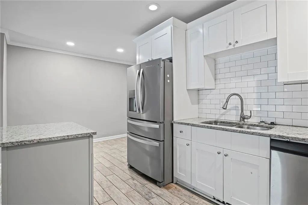 Kitchen with light stone countertops, stainless steel appliances, wood tiled floors, recessed lighting, and white cabinets