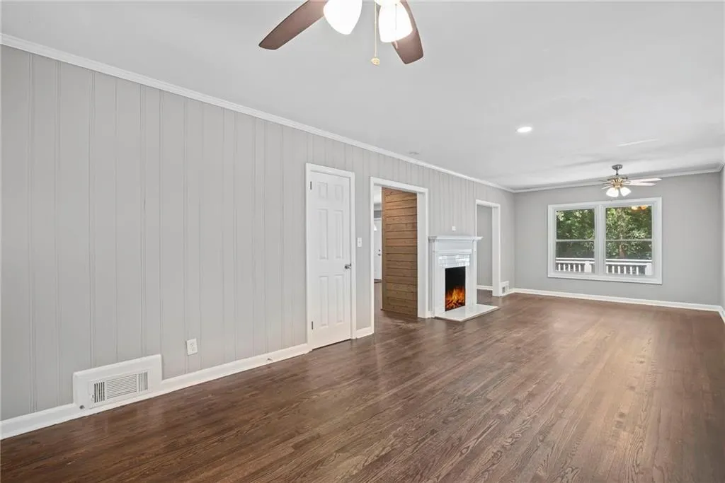 Unfurnished living room with a ceiling fan, ornamental molding, dark wood-style flooring, a lit fireplace, and wooden walls