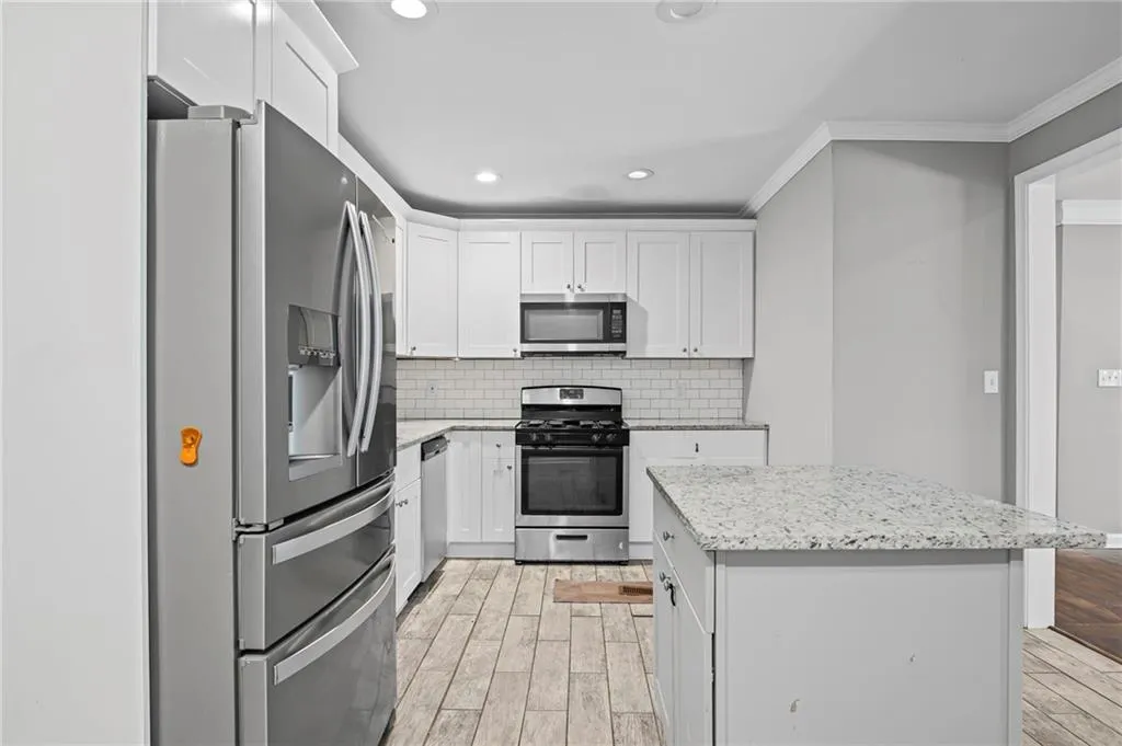 Kitchen featuring appliances with stainless steel finishes, wood tiled floors, decorative backsplash, white cabinetry, and recessed lighting