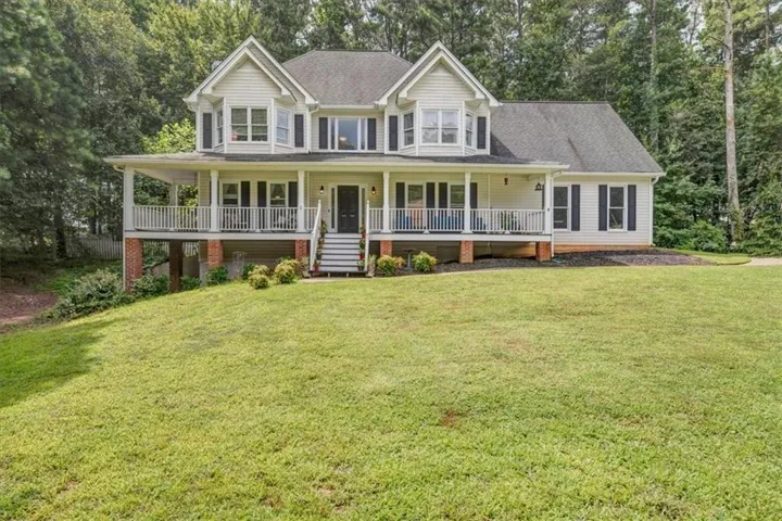 Two-story residence featuring a covered front porch with white railing, bay windows, dark shutters, and a front entry with steps
