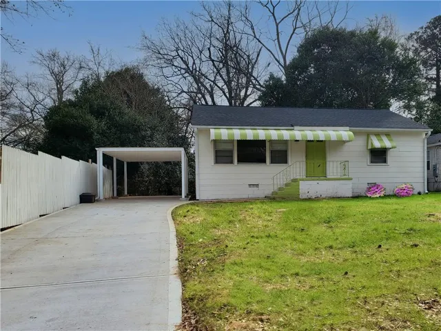 White exterior with striped awnings, a vibrant green front door, and a dedicated carport