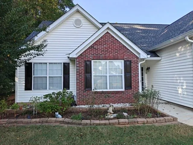 Red brick and white siding exterior with dark shutters, featuring a landscaped garden bed with block edging