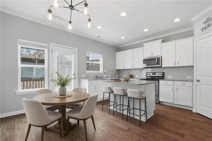Open-concept kitchen featuring white cabinetry, granite countertops, stainless steel appliances, hardwood flooring, and recessed lighting