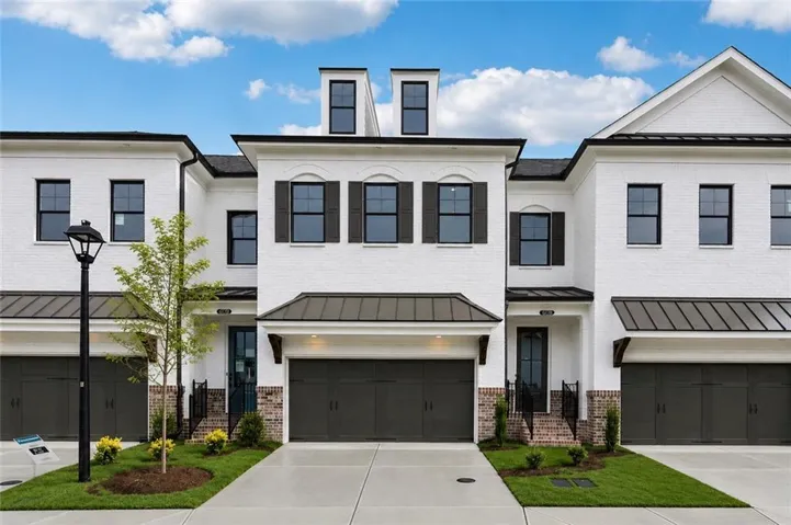 White brick exterior with black framed windows, dark garage doors, and metal roof accents