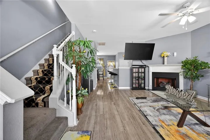 Living area with a fireplace with raised hearth, ceiling fan, and light wood-style flooring