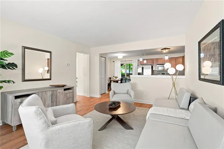 Living area with wood-finish flooring, light neutral wall tones, and a pass-through opening to the kitchen