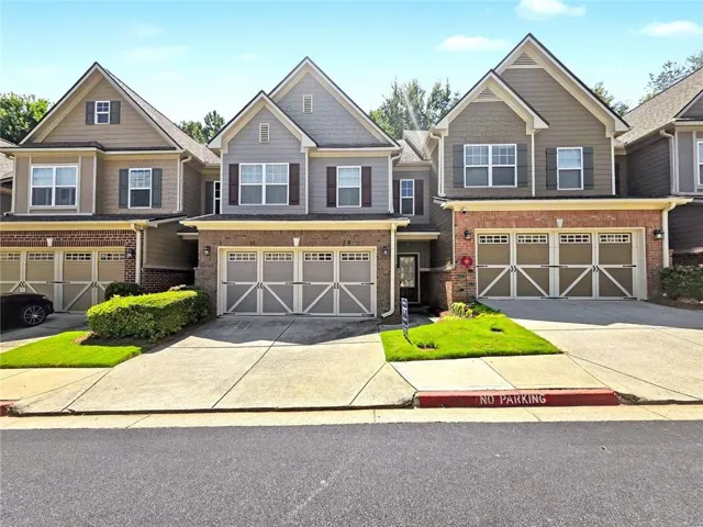 Two-story townhome featuring brick and siding exterior, an attached two-car garage with decorative doors, and a concrete driveway