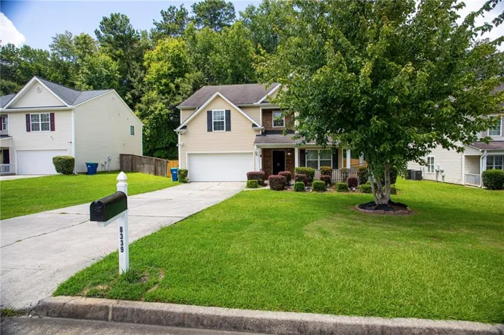 Two-story residence with a beige and brown exterior, featuring a white garage door and black shutters