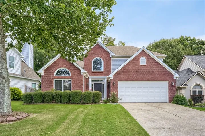 Brick and siding exterior with arched windows, a two-car garage, and a manicured lawn
