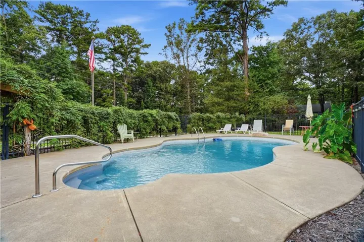 Freeform swimming pool with concrete decking, surrounded by mature trees and lush perimeter landscaping