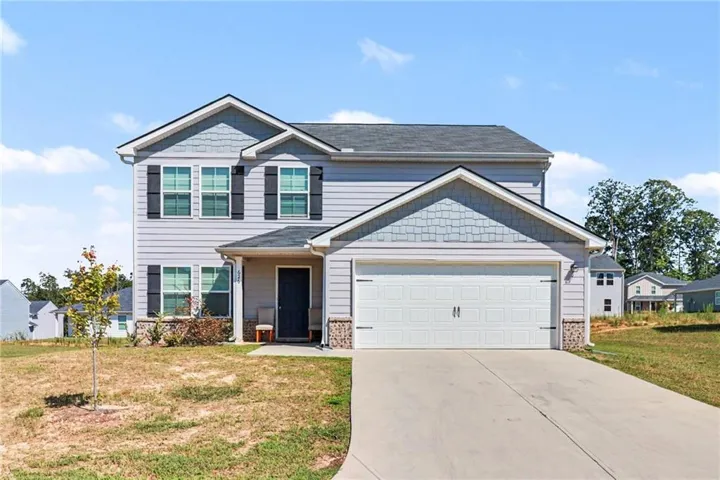 Two-story exterior with light gray siding, dark shutters, a two-car garage, and a concrete driveway