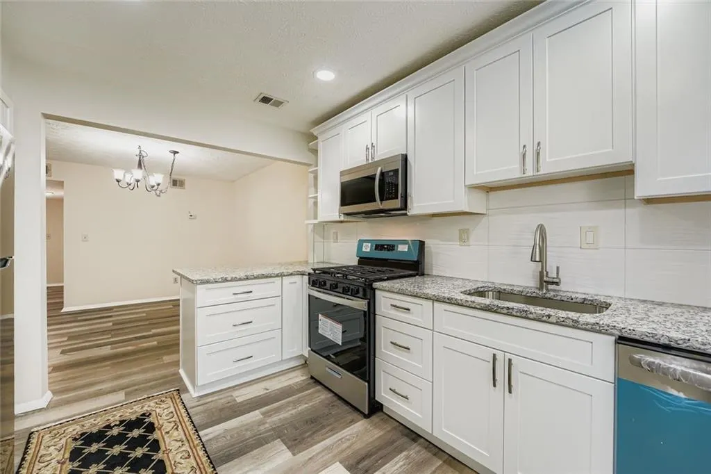 Kitchen with appliances with stainless steel finishes, backsplash, white cabinets, light stone countertops, and a textured ceiling