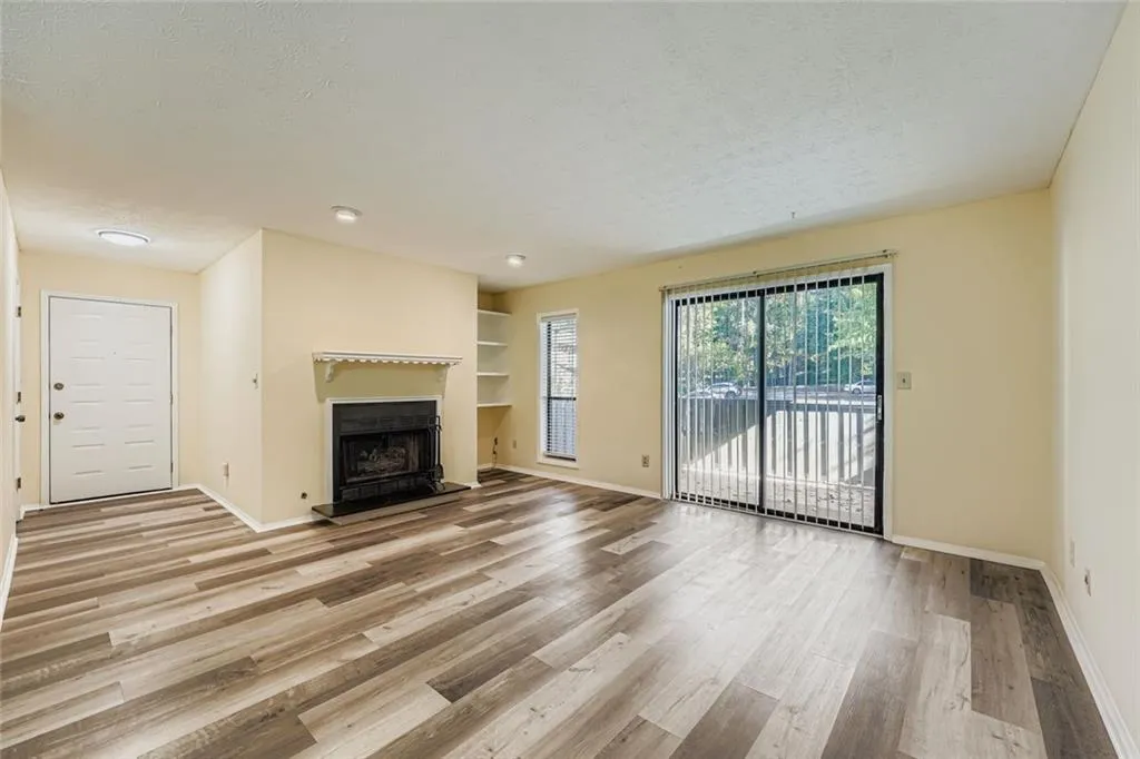 Unfurnished living room with light wood finished floors, a fireplace with raised hearth, a textured ceiling, and built in features