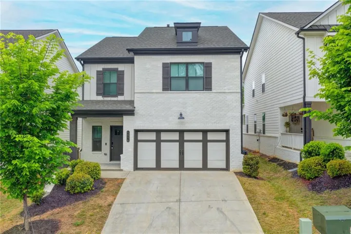 White brick and vertical siding exterior with dark trim accents, featuring a covered front entry and a two-car garage with frosted panels