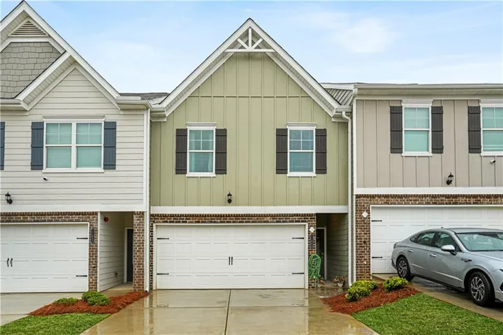Exterior featuring a light green facade with board and batten siding, brick accents, and black window shutters