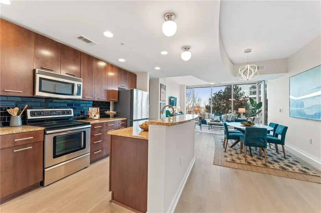 Kitchen featuring stainless steel appliances, an island with sink, light wood-type flooring, light stone counters, and expansive windows