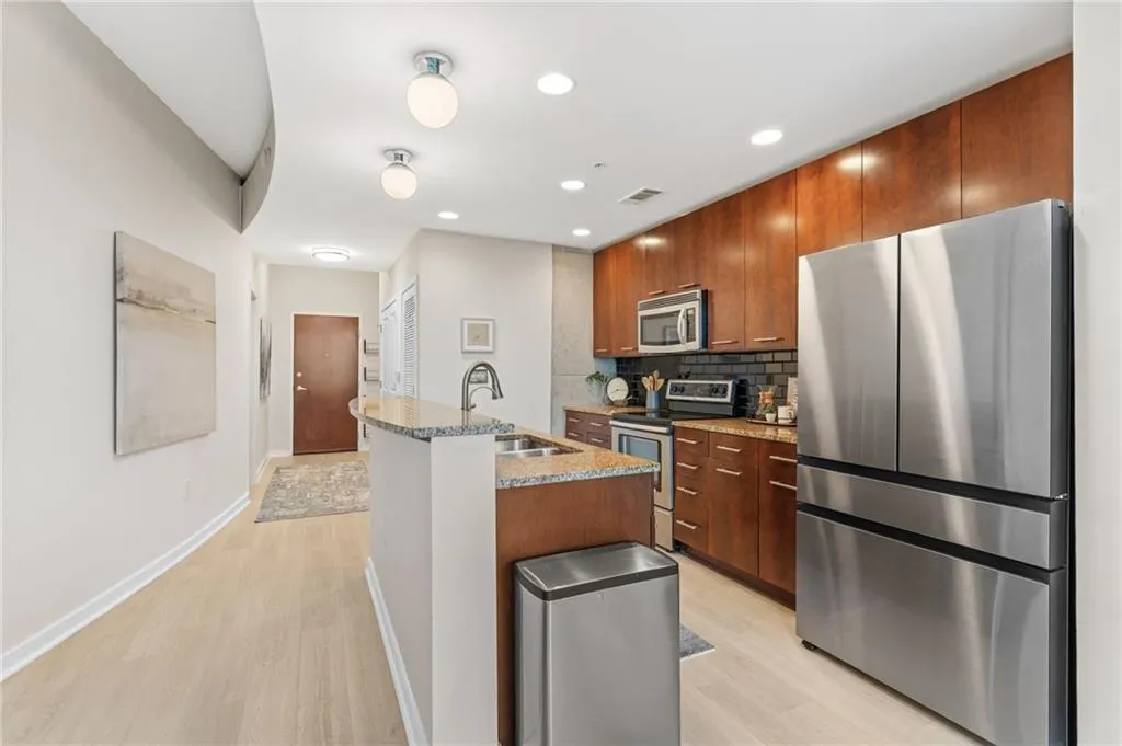 Kitchen with light stone countertops, stainless steel appliances, light wood-style floors, a center island with sink, and recessed lighting