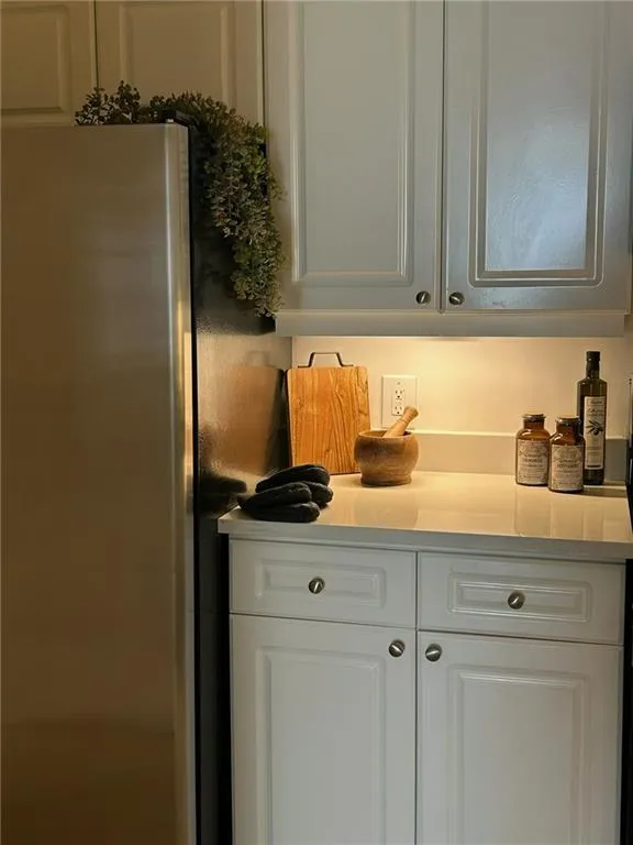 Stainless steel refrigerator, white shaker-style cabinetry, light-toned countertop, under-cabinet lighting