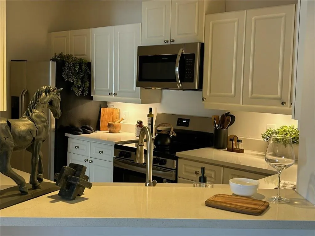 White shaker cabinetry, stainless steel appliances, light-toned countertops, and a gooseneck faucet
