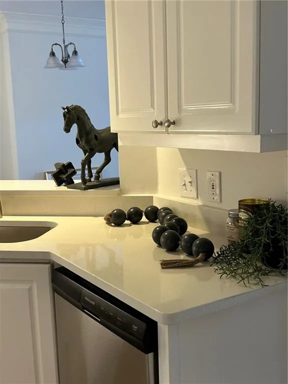 Light-toned countertops, white cabinetry with silver-tone hardware, undermount sink, stainless steel dishwasher