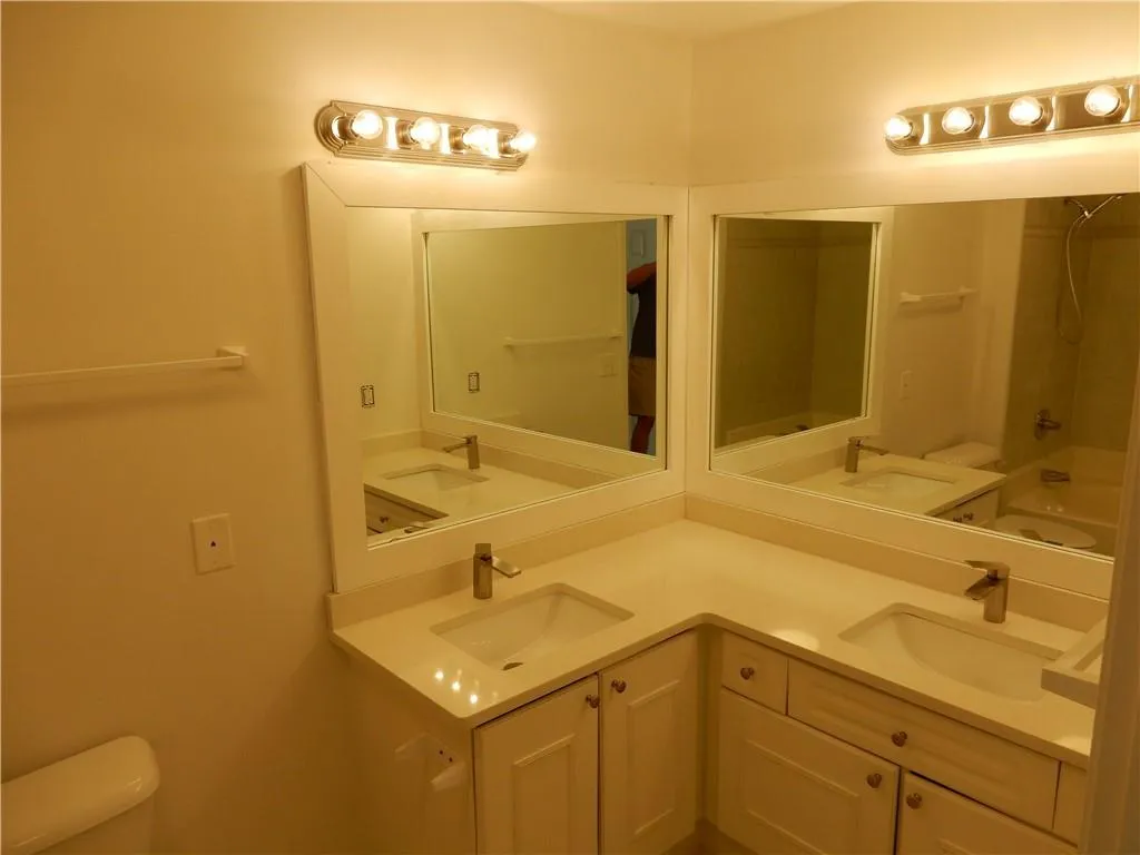 Dual vanity with integrated sinks, white cabinetry, chrome fixtures, and wall-mounted lighting