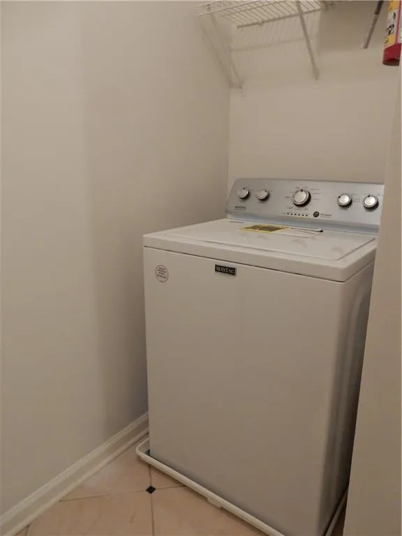 Compact laundry area featuring a white top-load washing machine, wire shelving, and tiled flooring