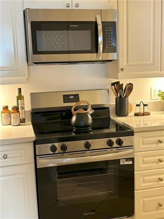Stainless steel over-the-range microwave and electric range with a black cooktop, complemented by white shaker-style cabinetry and light-toned countertops
