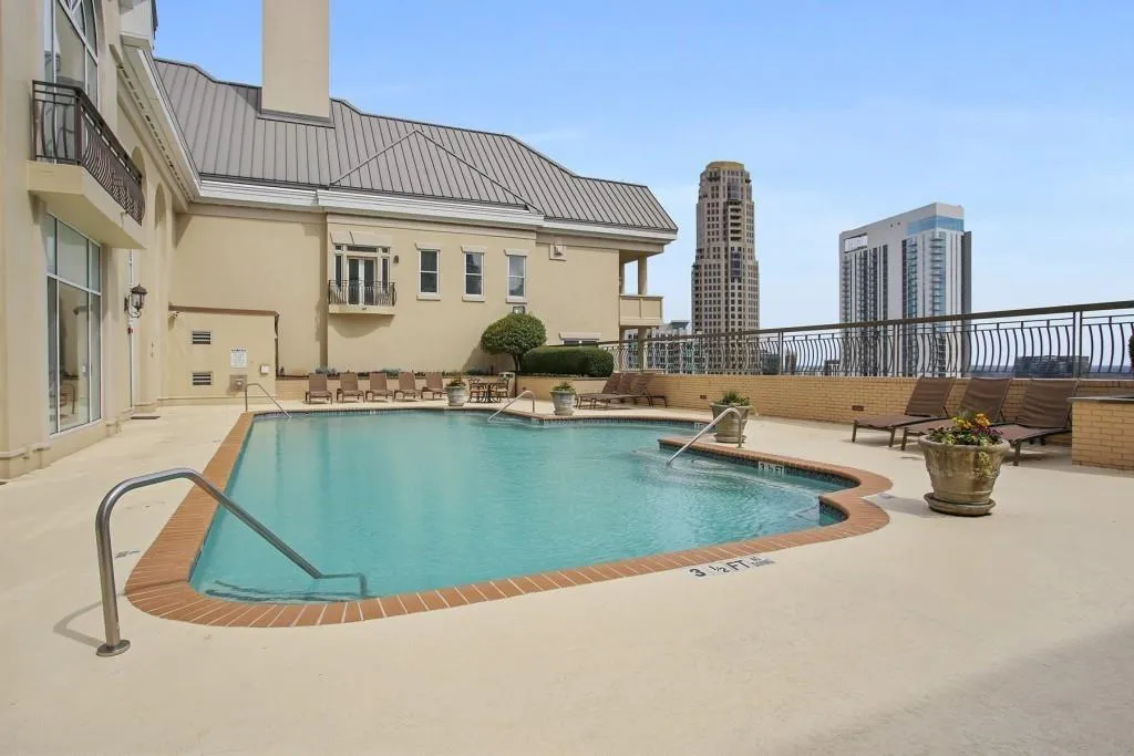 Rooftop swimming pool with integrated water feature, surrounded by a spacious paved deck, brick coping, and a metal railing