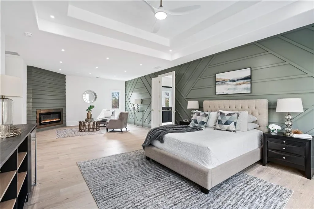 Bedroom featuring a fireplace, a tray ceiling, light hardwood / wood-style flooring, and ceiling fan Bedroom featuring a fireplace, a tray ceiling, light hardwood / wood-style flooring, and ceiling fan