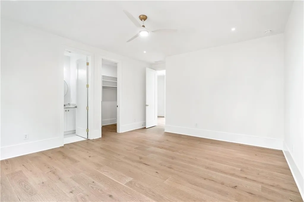 Unfurnished bedroom featuring ceiling fan, a spacious closet, ensuite bathroom, and light hardwood / wood-style flooring Unfurnished bedroom featuring ceiling fan, a spacious closet, ensuite bathroom, and light hardwood / wood-style flooring
