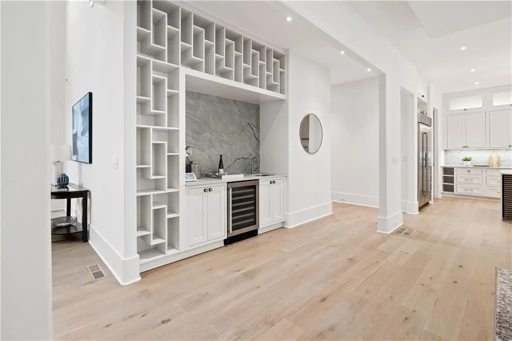 Bar featuring light wood-type flooring, backsplash, beverage cooler, sink, and white cabinets Bar featuring light wood-type flooring, backsplash, beverage cooler, sink, and white cabinets