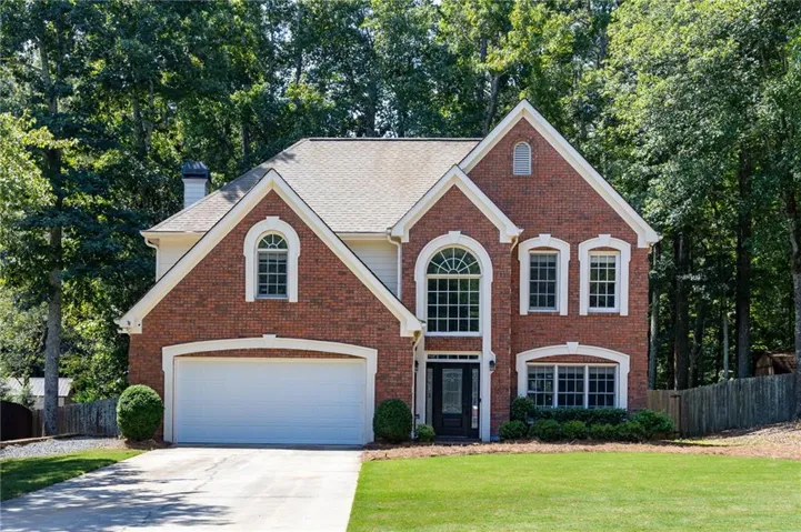 Brick exterior with white trim, arched and rectangular windows, a two-car garage, and a concrete driveway