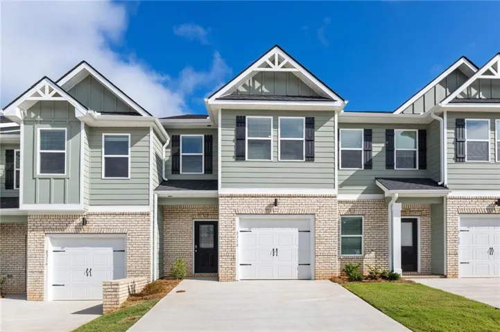 Contemporary townhome exterior featuring light brick and horizontal siding, decorative gables, black shutters, and an attached garage