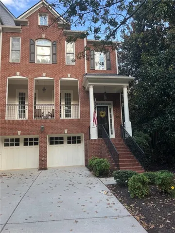 Three-story brick exterior with dual garage doors, columned portico, and two upper-level balconies with wrought iron railings