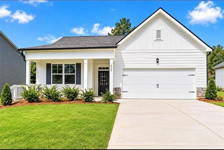 White siding exterior with a prominent front porch, dark-framed windows, and a two-car garage