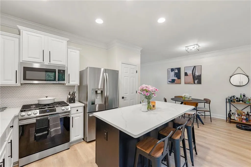 Kitchen with light hardwood / wood-style flooring, backsplash, stainless steel appliances, and a breakfast bar area