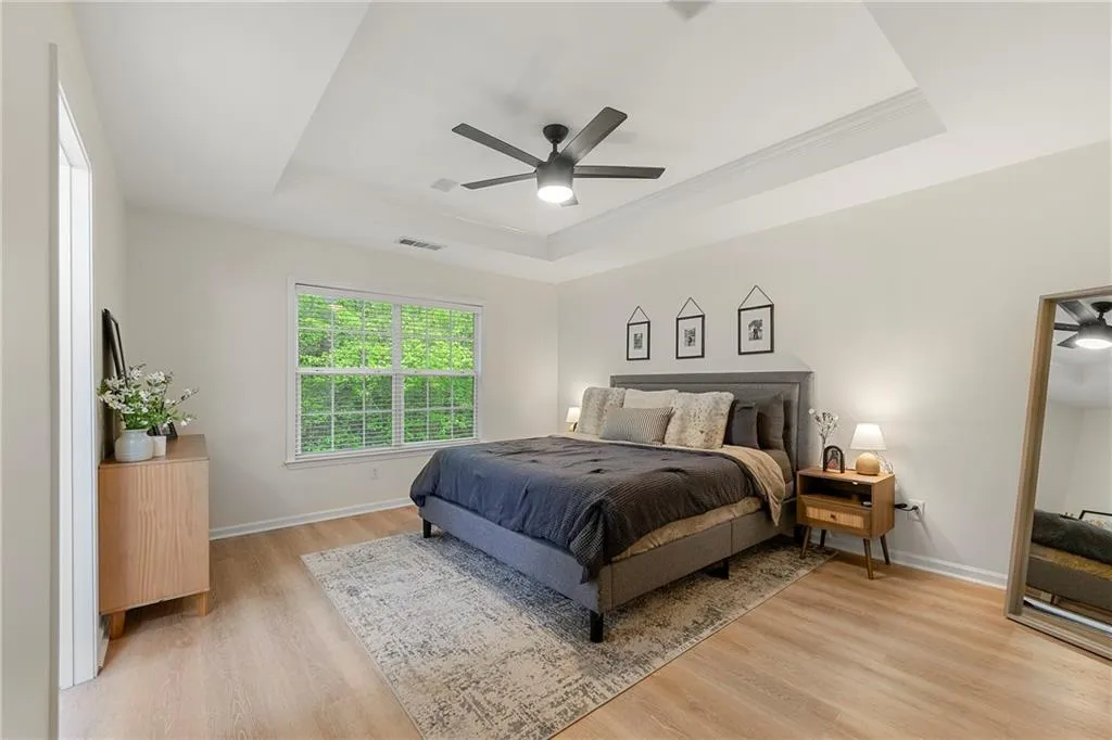 Bedroom featuring light hardwood / wood-style floors, ceiling fan, and a tray ceiling