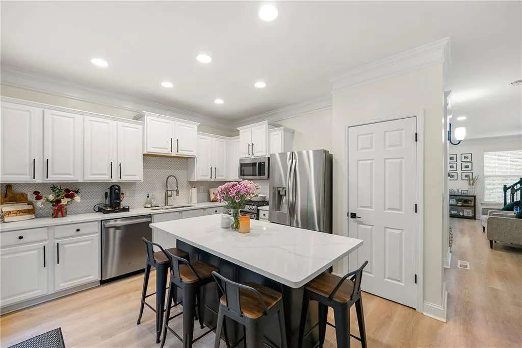 Kitchen with appliances with stainless steel finishes, white cabinets, sink, a breakfast bar area, and light hardwood / wood-style flooring